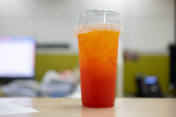 Clear plastic cup filled with ice fruit tea a lid on wood table