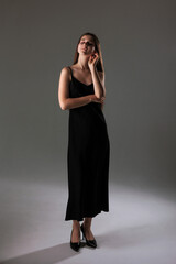 Fototapeta premium Elegant woman in a sleek black dress poses thoughtfully in a minimalist backdrop during a studio photoshoot