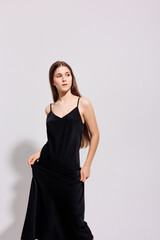 Naklejka premium Young woman posing gracefully in a sleek black dress against a simple backdrop in a studio setting