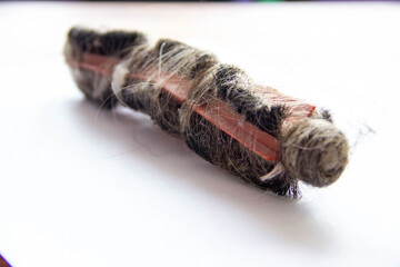 A dirty roller brush from a vacuum cleaner covered in hair, dust and fur. The brush has an orange body with black fluffy inserts that are clogged with debris.