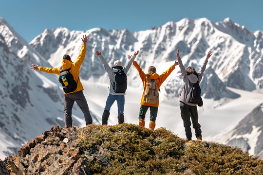 Group of happy young friends hikers are standing with open arms high in mountains against snow ridge with glacier