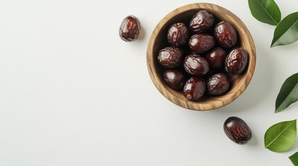Obraz premium Freshly harvested dates nestled in a rustic wooden bowl on a clean surface, surrounded by lush green leaves and natural light highlighting their rich texture