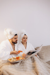 Couple Relaxing on Couch Enjoying Food and Sharing Book in Cozy Robes