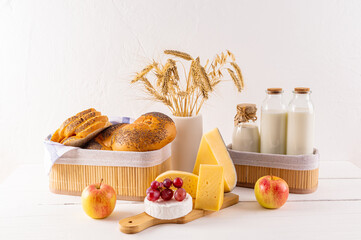 Freshly baked homemade bread, cheese, milk, apples on a white wooden table in stylish straw boxes. Traditional treats for the holiday of Shavuot.