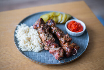 Grilled meat BBQ with rices, cucumber, salads and sauce served on stylish plate on wooden table
