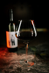 Elegant red wine glass with a bottle in dim light setting, perfect for an intimate gathering or celebration