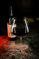 Dark red wine glass with reflections and a bottle in the background at a dimly lit setting