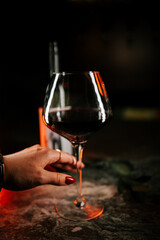 Elegant glass of red wine held by a hand in a dimly lit setting with soft shadows and warm tones in the background