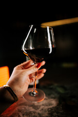 Elegant hand holding a glass of red wine in a dimly lit bar setting during the evening