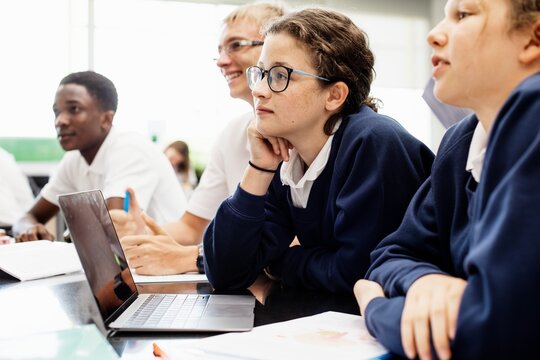 Diverse group of students in a classroom. Students including a girl, engaged in learning. Classroom setting with students focused on a laptop. Students listening in science and math classroom.
