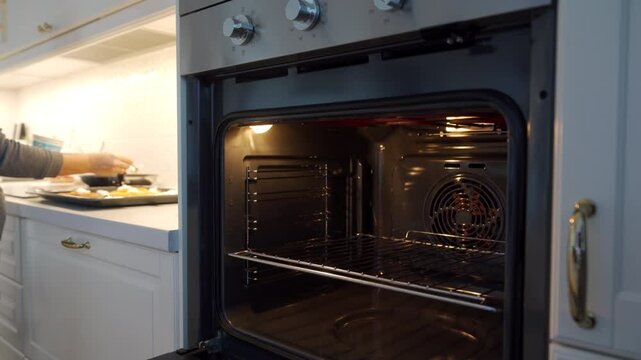 Woman cooking on countertop in the kitchen at home. Electric oven with door open is preheating before baking dish.