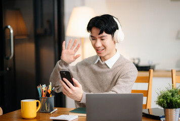 Young Asian man with sitting working on laptops and tablets in a cozy workspace. Perfect for education, innovation, and remote work themes