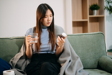 Young Asian woman suffering from flu symptoms, covered with a blanket on a sofa. Concept of...