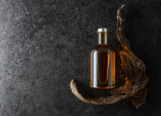 Bottle of whiskey and old snags on a black stone background.