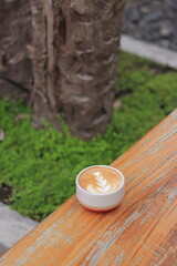 Latte Art Enhances Coffee Experience with Nature Background, Rustic Table, and Greenery