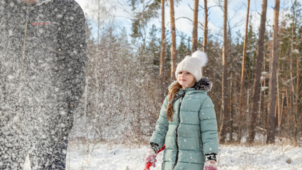 Little girls play with snow with her grandfather in winter forest