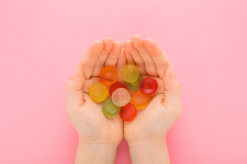 Little child girl opened palms holding colorful jelly gummy candies on light pink table background. Pastel color. Sweet snack. Closeup. Point of view shot. Top down view.