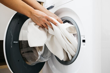 A woman's hand takes freshly washed clothes from the washing machine in the bathroom. Concept: dry...