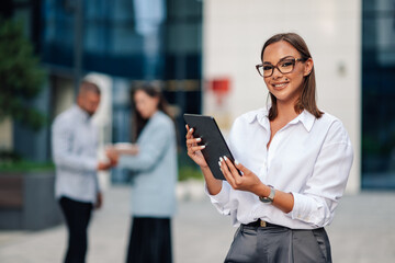 Fototapeta premium Businesswoman smiling holding digital tablet outside office building