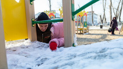 Grandfather playing with his granddaughter on the playground in the park in winter
