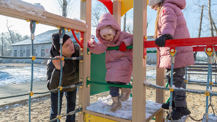 Grandfather with grandchildren playing on the playground on a cold winter day