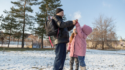Grandfather walks with his granddaughters after school in the park in sunny winter day