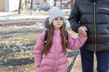 Grandfather walks with his granddaughters after school in the park in sunny winter day