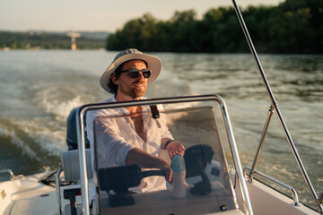 Young man enjoying a leisurely sunset cruise on a river, skillfully navigating a motorboat while...
