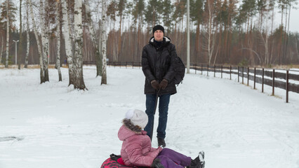Father pulling child girl sitting on inflatable tube in snow (inflatable sled)