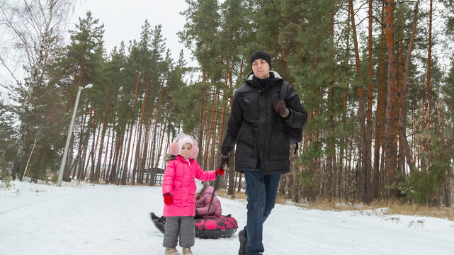 Father and daughters ride downhill on a Snow tubing in the park on the winter holidays