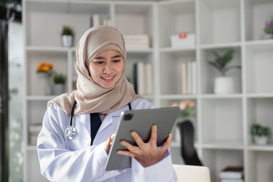 Engaged Muslim female doctor using a tablet to review patient information in a modern healthcare office, emphasizing technology and diversity.