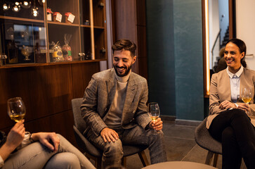 Group of business people sitting in hotel lobby chatting and drinking wine.