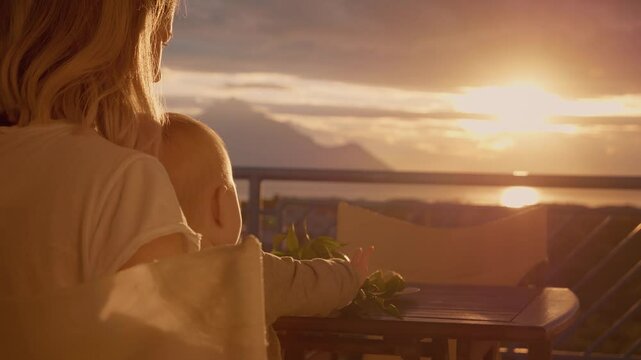Mother and son relaxing at the terrace looking at sunset. Silhouette of mom holding baby at sunset view from balcony.