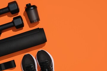 Black exercise equipment, dumbbells, mat, elastic band, fitness band, bottle and sneakers on orange...