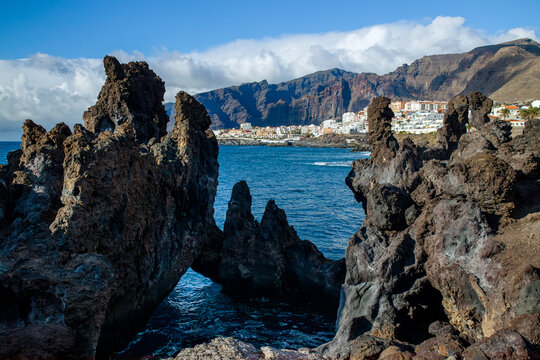 Charco La Vaca in Tenerife, Spain. Charcos Los Turistas park with lava rock formations and cave in the ocean. Los Gigantes seen in the distance.
