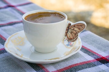 Cup of Turkish coffee served in a decorative porcelain cup with a butterfly design, placed on a plaid tablecloth.