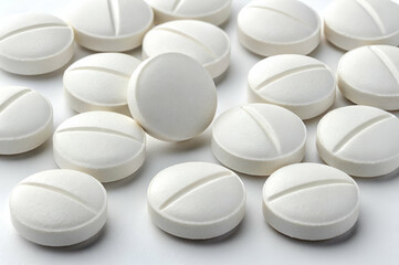 A collection of white, round pills scattered on a surface, showcasing their smooth texture and distinct line along the middle.