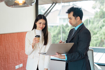Collaborative Asian business team discussing project details with a laptop and coffee in a modern office