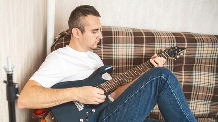 Musical hobby. Guitar skill. Man sitting on sofa playing string instrument enjoying learning chords...