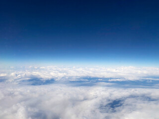 Expansive aerial view of white clouds stretching to the horizon under a deep blue sky. The high-altitude perspective captures the beauty of air travel and nature.
