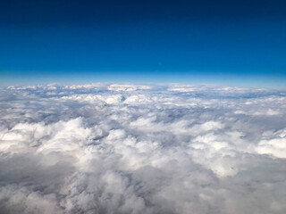 Expansive aerial view of white clouds stretching to the horizon under a deep blue sky. The high-altitude perspective captures the beauty of air travel and nature.