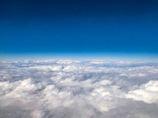 Expansive aerial view of white clouds stretching to the horizon under a deep blue sky. The high-altitude perspective captures the beauty of air travel and nature.