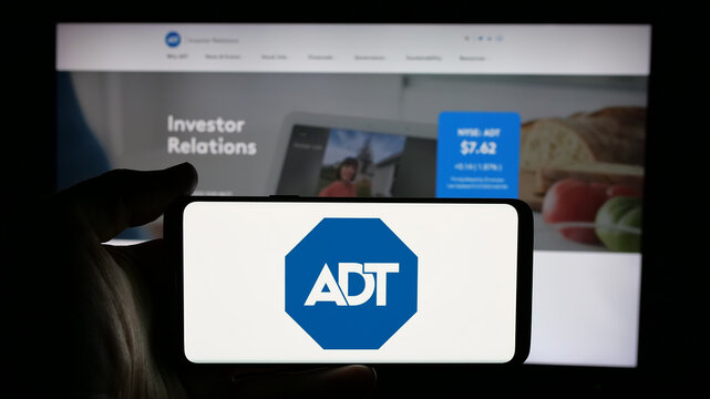 Stuttgart, Germany - 01-28-2025: Person holding cellphone with logo of US security company ADT Inc. on screen in front of business webpage. Focus on phone display.