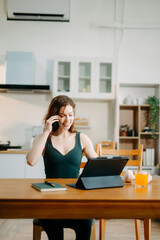 Happy woman with headphones working on a tablet in a bright kitchen. Ideal for themes of remote work, freelancing