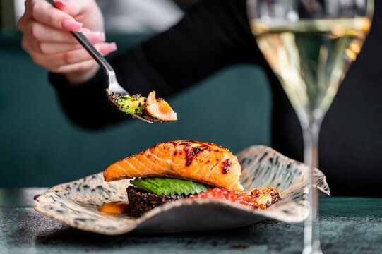 A gourmet dish featuring grilled salmon served on a decorative plate. The meal is complemented by a glass of wine, showcasing a sophisticated dining experience.