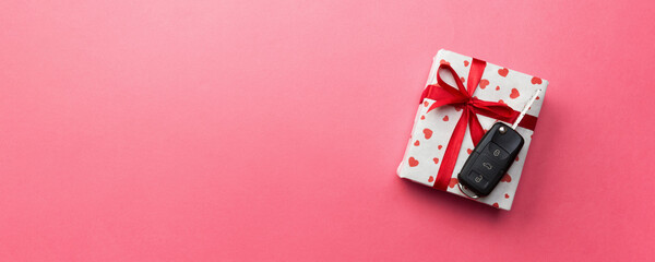 Car key on paper gift box with red ribbon bow and heart on pink table background. Holidays present top view concept