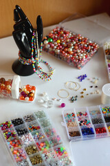 Hand figurine, colorful friendship bracelets, necklaces, various beads and DIY supplies on the table. Making jewelry at home. Selective focus.