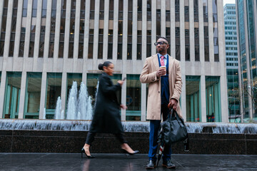 Stylish businessman holding coffee outside plaza with businesswoman walking by