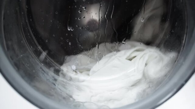 A washing machine filled with white laundry, in action. Concept: utilizing modern technology and cleaning services to simplify household chores and maintain order.