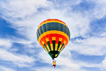 Colorful hot air balloon flying over blue sky with white clouds	